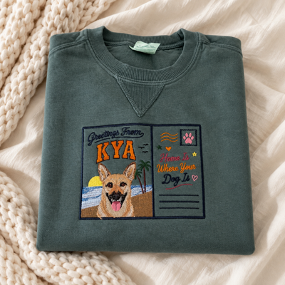 Custom embroidered pet portrait sweatshirt in Blue Spruce with a Greetings From Kya postcard design and dog portrait