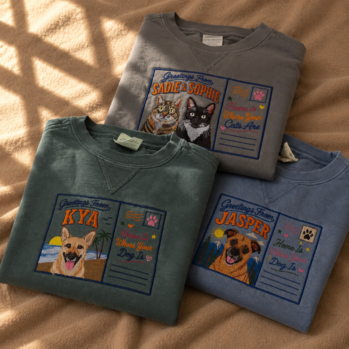Three custom embroidered pet portrait postcard sweatshirts in Pepper, Blue Spruce and Blue Jean with Greetings From dog and cat designs